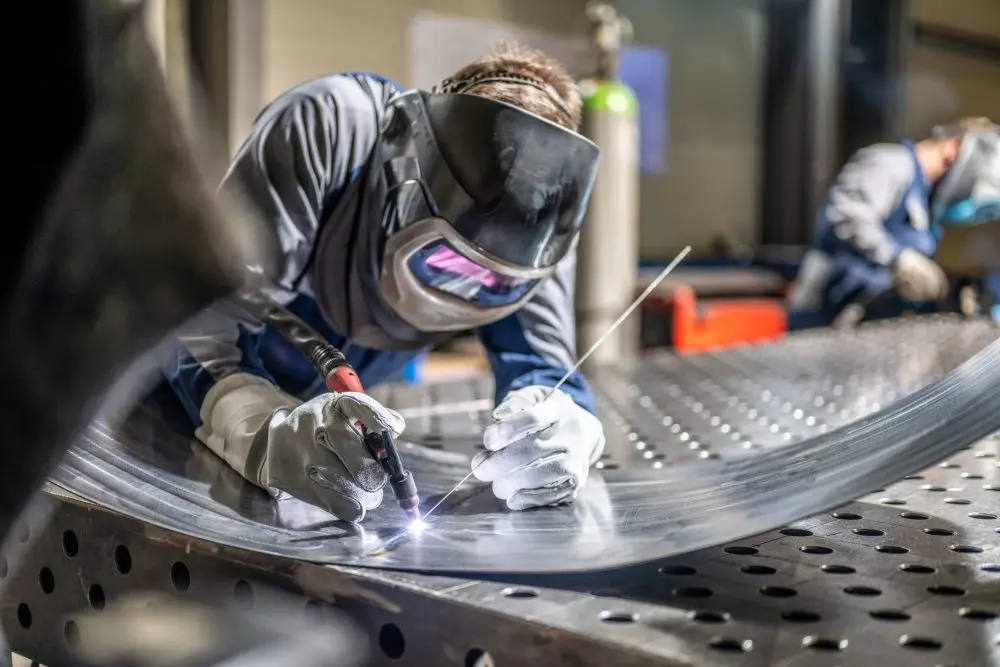 Soldador masculino con casco trabajando con soplete de soldadura en fábrica.